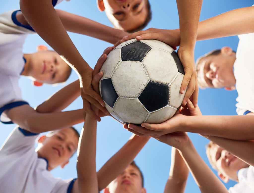 Mehrere kleine Kinder versammeln sich im Freien, halten aufgeregt einen Fußball in der Hand und haben ein strahlendes Lächeln im Gesicht.