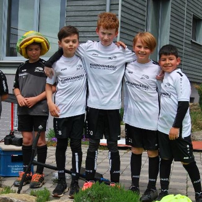 Fünf junge Jungen in bunten Fußballuniformen posieren fröhlich für ein Gruppenfoto.