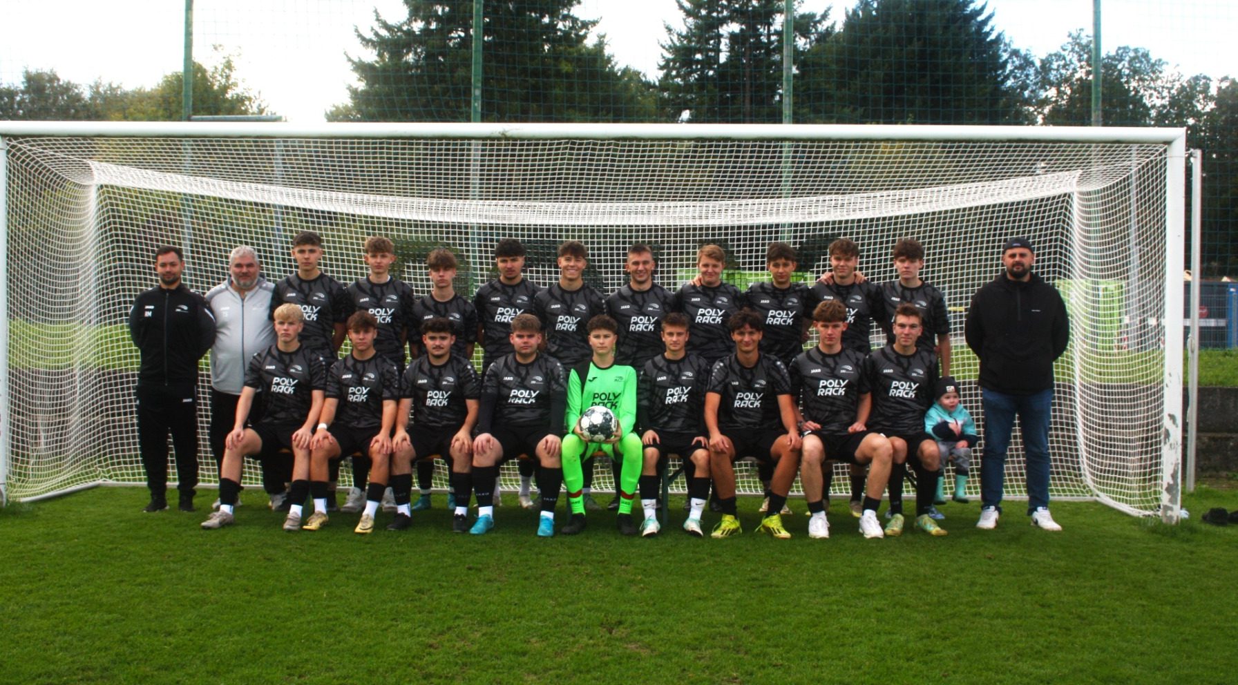Eine Fußballmannschaft posiert lächelnd vor einem Tor für ein Gruppenfoto.