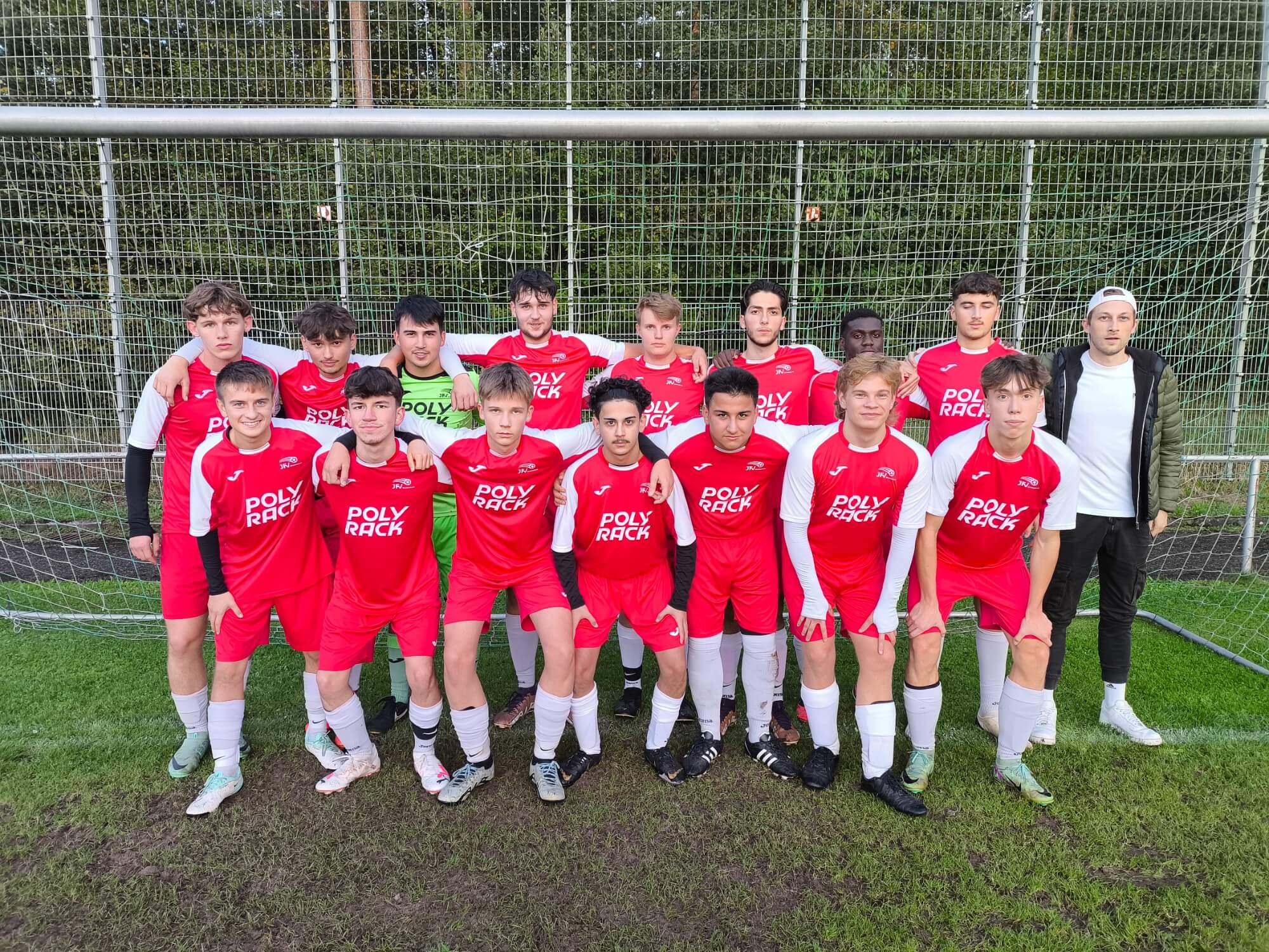 Fünf junge Männer in roten Fußballuniformen posieren lächelnd auf dem Platz.